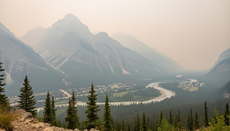 Canmore mountain peaks are partially obscured by wildfire smoke haze from a viewpoint.