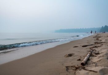 “Hazy Sauble Beach shoreline with muted colors and reduced visibility over the water from wildfire smoke.”
