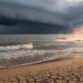 Storm clouds over a turbulent ocean with visible heat haze and cracked ground in the foreground, symbolizing extreme weather amplification.